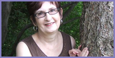 A woman with glasses standing next to a tree.